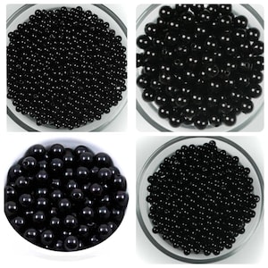 May include: Four images displaying black, spherical beads in clear glass bowls. The beads are consistent in size and have a shiny surface. The bowls are arranged in a square, providing varied views of the beads.