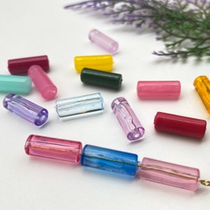 May include: Assortment of colorful glass beads in various shapes and sizes. The beads are arranged on a white surface.