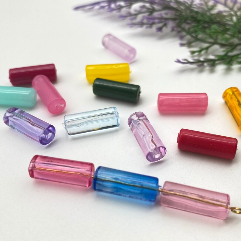 May include: Assortment of colorful glass beads in various shapes and sizes. The beads are arranged on a white surface.