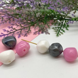 K&ouml;nnte beinhalten: Nahaufnahme einer Perlenkette. Die Perlen sind rosa, wei&szlig; und grau. Die Perlen sind aus Kunststoff und haben eine gl&auml;nzende Oberfl&auml;che.