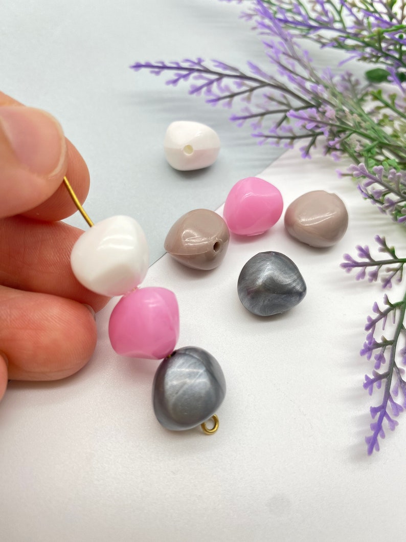 K&ouml;nnte beinhalten: Sortiment an bunten Plastikperlen in Rosa, Wei&szlig; und Grau. Die Perlen sind tropfenf&ouml;rmig und haben ein Loch in der Mitte zum Auf f&auml;deln.