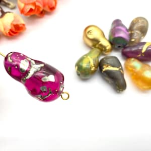 Pode incluir: Conjunto de contas de vidro em forma de pêra com detalhes dourados. As contas são de várias cores, incluindo roxo, verde, dourado e marrom. As contas têm um acabamento perolado e são perfeitas para a fabricação de joias.