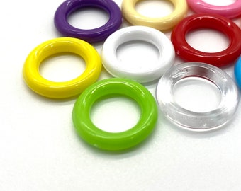 Puede incluir: Surtido de anillos de plástico de colores, incluyendo amarillo, verde, morado, blanco, rojo, rosa y transparente. Los anillos son todos del mismo tamaño y forma, y están dispuestos en círculo.
