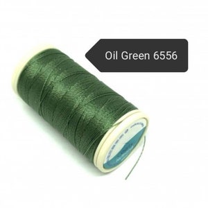 May include: A spool of oil green thread, color code 6556, is displayed against a white background. The thread is tightly wound around a white and beige spool. The image is well-lit, highlighting the thread's texture and color.