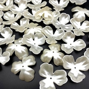 May include: A scattering of ivory-coloured, five-petal flower-shaped beads. Each bead has a pearlescent sheen and a small hole in the centre. These craft supplies are ideal for jewellery making and embellishments.