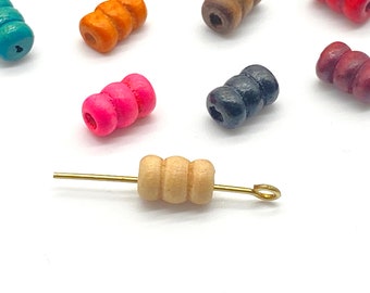 May include: A close-up of a wooden bead with a gold wire attached. The bead is light brown and has three ridges. The bead is surrounded by other beads of various colors, including pink, blue, red, and orange.