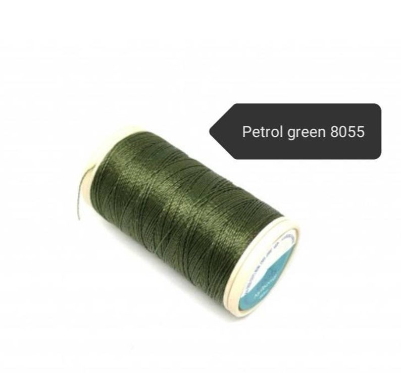 May include: A spool of petrol green thread, color code 8055, against a white background. The thread is tightly wound on a cardboard spool with a white and blue label. The thread has a slight sheen.