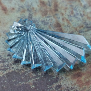 Könnte beinhalten: Ein hellblauer Kristall-Sonnenstrahl-Anhänger mit facettiertem Design. Der Anhänger ist aus Glas und hat ein zartes, filigranes Muster.