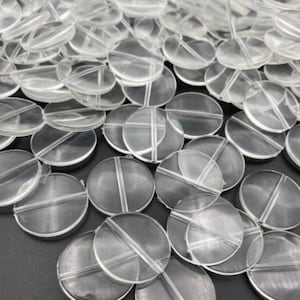 May include: A collection of clear, circular plastic pieces, each with a cross-shaped design. The pieces are stacked together, creating a textured surface. The transparent material allows light to pass through, highlighting the details of the design.