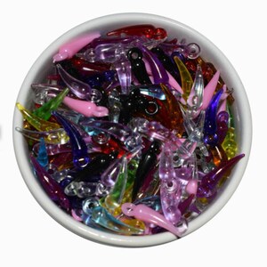 May include: A white bowl filled with a variety of colorful, transparent, teardrop-shaped beads. The beads are in shades of pink, red, black, green, purple, and blue. These beads are likely used for jewelry making or other craft projects.