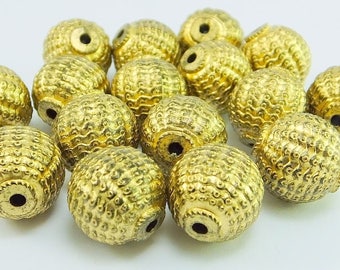 May include: A pile of 18 gold-colored metal beads with a textured surface. The beads are round and have a hole in the center.