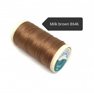 May include: A spool of milk brown thread, color code 8646, is shown. The thread is tightly wound around a white and teal spool. The thread is a light brown color.