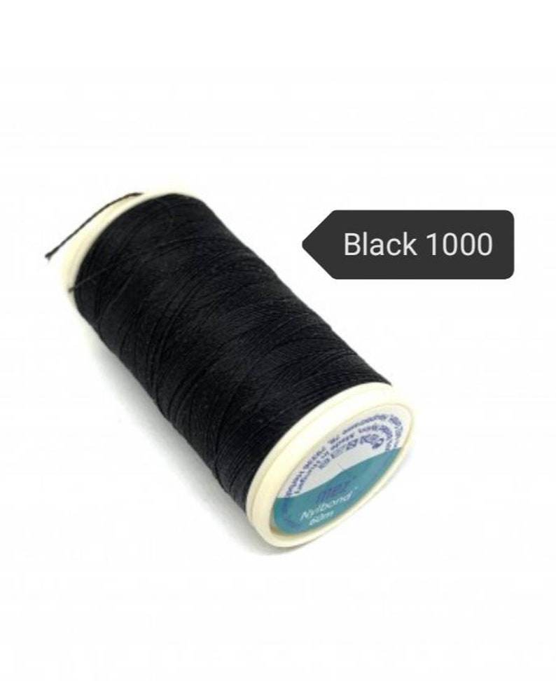 May include: A spool of black thread labeled "Black 1000". The thread is tightly wound around a white and blue spool. The thread is a deep black color, and the spool has a white rim.