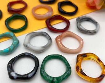 May include: A collection of 12 colorful resin rings with unique irregular shapes. The rings are made of different colors, including black, white, red, green, blue, and brown.