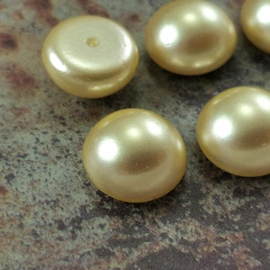May include: A group of six pearl-like buttons in a pale yellow color. The buttons are round and have a smooth, glossy finish.