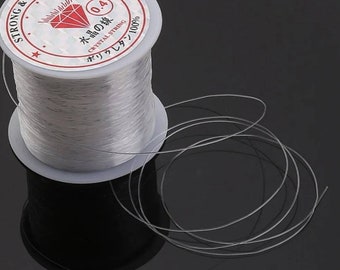 Puede incluir: Un carrete de hilo elástico transparente con una etiqueta que dice "Strong & Stretchy 0.4 水田の線 Crystal String オリカレタ 100%"