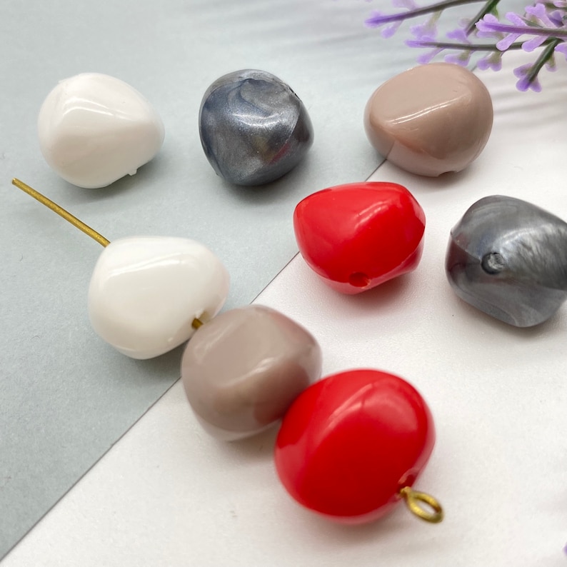 K&ouml;nnte beinhalten: Sortiment aus sechs Plastikperlen in verschiedenen Farben, darunter Wei&szlig;, Grau, Braun und Rot. Die Perlen sind glatt und haben eine leicht unregelm&auml;&szlig;ige Form.