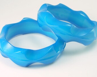 May include: Two blue plastic bangles with a wavy design. The bangles are stacked on top of each other.