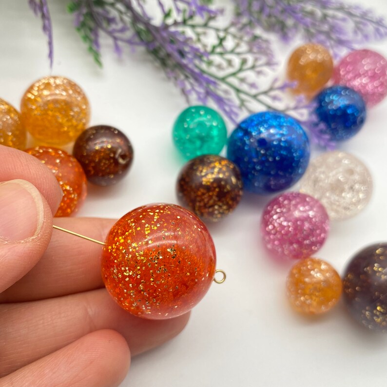 Puede incluir: Surtido de cuentas redondas de colores con purpurina incrustada en resina transparente. Las cuentas son de varios colores, incluyendo naranja, marr&oacute;n, azul, verde, rosa y transparente.