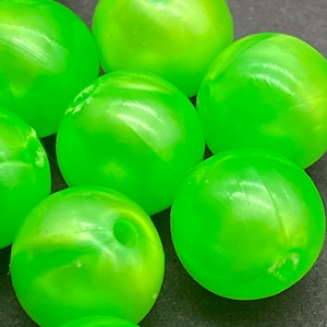 May include: A group of bright green, shiny, round beads with a hole in the center. The beads are made of a translucent material and have a slight iridescent sheen.