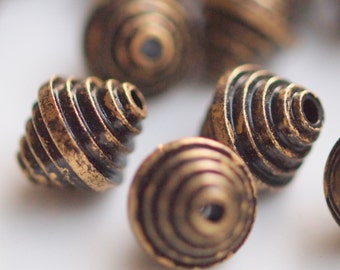 Puede incluir: Una colección de cuentas de metal dorado y negro con un diseño en espiral y círculos concéntricos. Las cuentas tienen un acabado desgastado y antiguo.