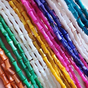 Op de afbeelding: Een verzameling kleurrijke kralen in bamboevorm in verschillende tinten, waaronder oranje, groen, wit, geel, roze, blauw en blauwgroen. De kralen zijn in parallelle rijen gerangschikt, waardoor een levendige en gestructureerde weergave ontstaat. Deze kralen zijn geschikt voor het maken van sieraden en knutselen.