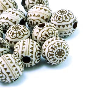Puede incluir: Una colección de cuentas de madera blancas con patrones geométricos marrones. Las cuentas tienen un agujero en el centro para enhebrar.