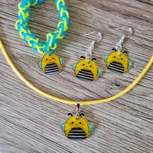 May include: A set of bee-themed jewellery, including a necklace, earrings, and a bracelet. The necklace and earrings feature a yellow and black bee charm with a smiling face. The bracelet is made of blue and green rubber bands.