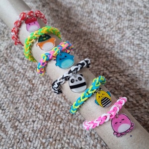 May include: A set of colourful rubber band bracelets with cute cartoon charms. The charms include a panda, a bee, a mushroom, a fish, and an octopus. The bracelets are made of rainbow-coloured rubber bands.
