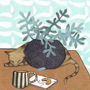 Op de afbeelding: Een bruine en witte kat slaapt op een tafel met een zwart-wit gestreepte mok en een koekje op een witte envelop. Een blauwe, bladerrijke plant staat in een zwarte pot achter de kat.