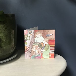 Pu&ograve; includere: Un biglietto d'auguri con un'illustrazione di due bambini che guardano dentro un cassetto di una cassettiera con tre gattini dentro. Il cassetto &egrave; aperto e i bambini sorridono. La carta ha uno sfondo a righe colorato.