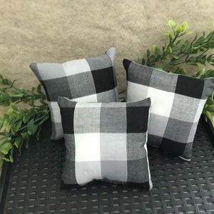 May include: Three square throw pillows featuring a black, white, and gray buffalo check pattern. The pillows are arranged in a cluster, showcasing the repeating grid design on the fabric covers. Each pillow has a soft, stuffed appearance.