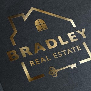 A gold foil logo on a dark gray background, showing a house outline, the text "BRADLEY REAL ESTATE," and a vintage key.