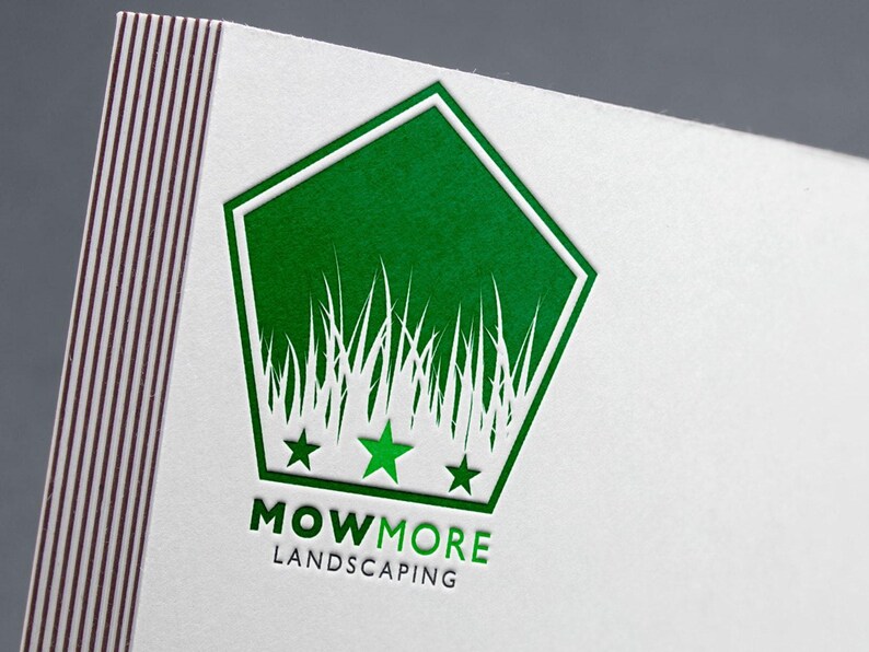 A close-up of a white business card with a green foil-stamped pentagonal logo featuring grass, three stars, and "MOWMORE LANDSCAPING" text.