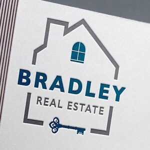 A white business card with a blue and gray logo featuring a house outline, the text "BRADLEY REAL ESTATE," and a vintage key.