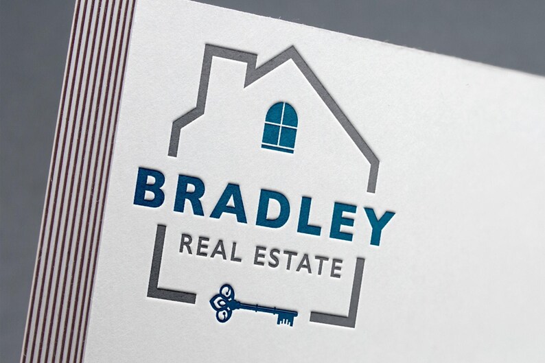 A white business card with a blue and gray logo featuring a house outline, the text "BRADLEY REAL ESTATE," and a vintage key.