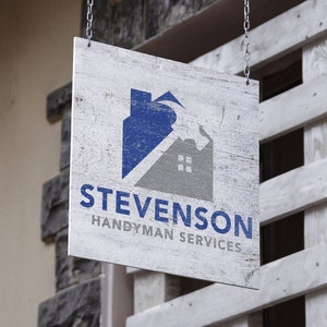 Puede incluir: Un letrero de madera blanco con un logotipo de casa azul y gris y el texto "Stevenson Handyman Services".