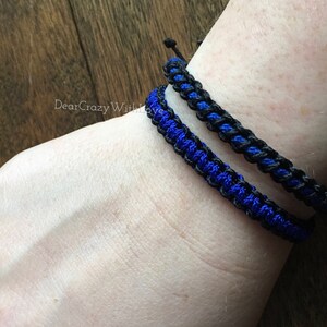 Puede incluir: Dos pulseras trenzadas, una negra y otra azul, puestas en la mu&ntilde;eca.