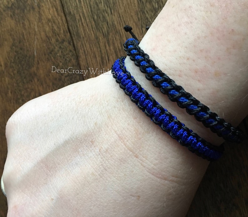 Puede incluir: Dos pulseras trenzadas, una negra y otra azul, puestas en la mu&ntilde;eca.