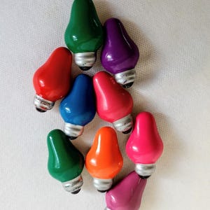 Peut inclure: Un ensemble d'ampoules de Noël colorées en forme de goutte d'eau. Les ampoules sont de différentes couleurs, notamment rouge, vert, bleu, orange, rose et violet. Chaque ampoule a une base argentée.