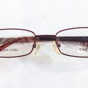 Op de afbeelding: Rechthoekige bril met een bordeauxrood montuur en pootjes. De lenzen zijn helder en de neuspads zijn beige. De tekst "STAINLESS STEEL" is zichtbaar aan de linkerkant van het montuur en "UNIVO" aan de rechterkant.