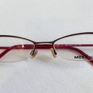 May include: A pair of eyeglasses with a brown and red frame. The glasses have a half-rim design with clear lenses. The brand name "MEXX titan" is visible on the right lens.