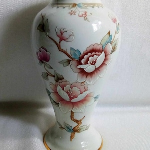 May include: A white ceramic vase with a floral design. The vase has a gold rim and a delicate floral pattern in shades of pink, blue, and green.