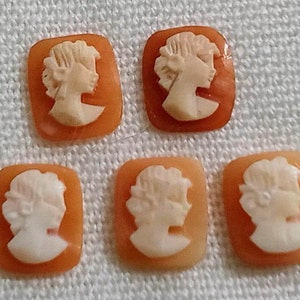 May include: Six small, square, cameo-style pendants in orange and white. Each pendant features a white cameo of a woman's profile.