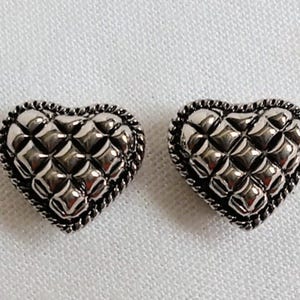 Peut inclure: Deux ornements argentés en forme de cœur. Chaque cœur présente un motif matelassé et une bordure en forme de corde. Les cœurs sont présentés sur une surface blanche et texturée. Ces éléments décoratifs peuvent être utilisés pour des bijoux ou des projets d'artisanat.