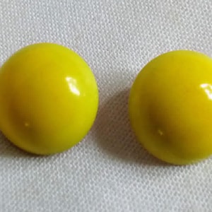 May include: A pair of yellow round earrings. The earrings are made of a smooth, shiny material.