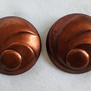 May include: A pair of copper-coloured earrings with a swirling, abstract design.