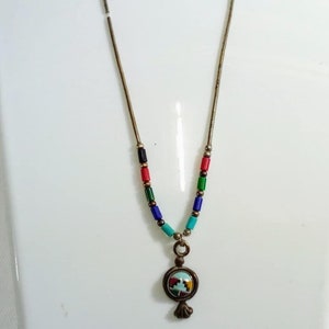 Peut inclure: Un collier en chaîne argent avec un pendentif rond orné d'une mosaïque colorée. Le pendentif est attaché à la chaîne par une petite boucle argentée.