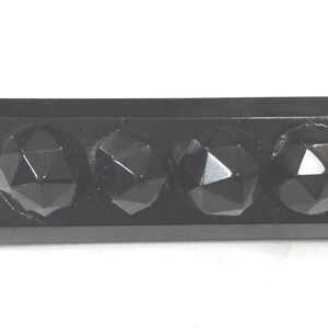 May include: A rectangular, black decorative object featuring four faceted, spherical shapes. The spheres have a geometric design and reflect light, creating highlights. The object is likely a decorative element or hardware.