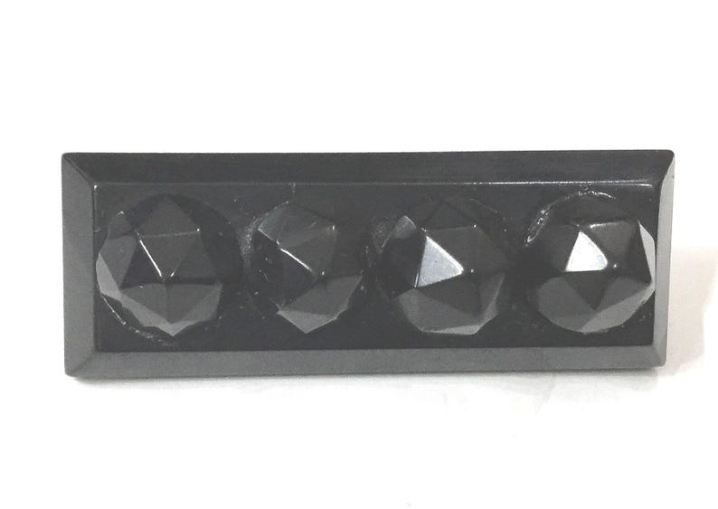 May include: A rectangular, black decorative object featuring four faceted, spherical shapes. The spheres have a geometric design and reflect light, creating highlights. The object is likely a decorative element or hardware.